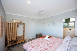 Une chambre à coucher avec un lit, une armoire, un ventilateur de plafond et une salle de bain visible à travers une porte ouverte.