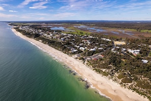 Vue aérienne d’une zone résidentielle côtière, avec des maisons le long de la plage, des routes et des terrains ouverts.