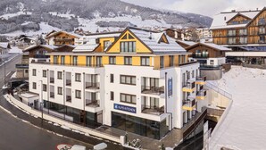 A multi-story hotel with balconies, a sign for 'Alps Kitchen', and a view of snow-covered mountains. - Modern Apartment With Balcony (Fiss)