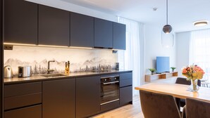 A modern kitchen with dark cabinets, a built-in oven, and a wooden dining table with chairs. - Modern Apartment With Balcony (Fiss)