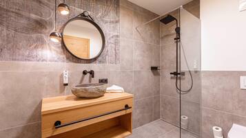 A modern bathroom with a wooden vanity, a round mirror, a stone sink, a glass-enclosed shower, and a toilet.