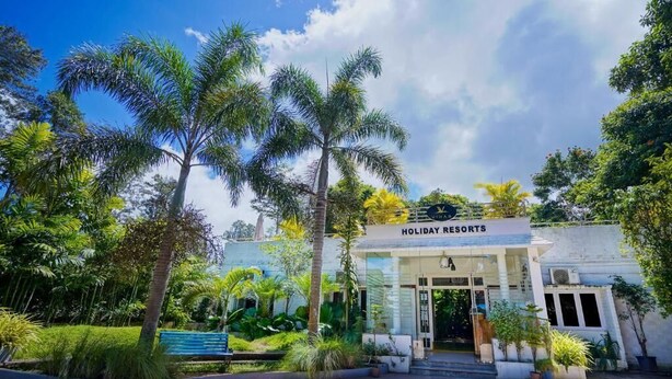 A building labeled "Holiday Resorts" with a clear entrance, surrounded by lush greenery and palm trees. - Vihar Holiday Resorts (Araku Valley)