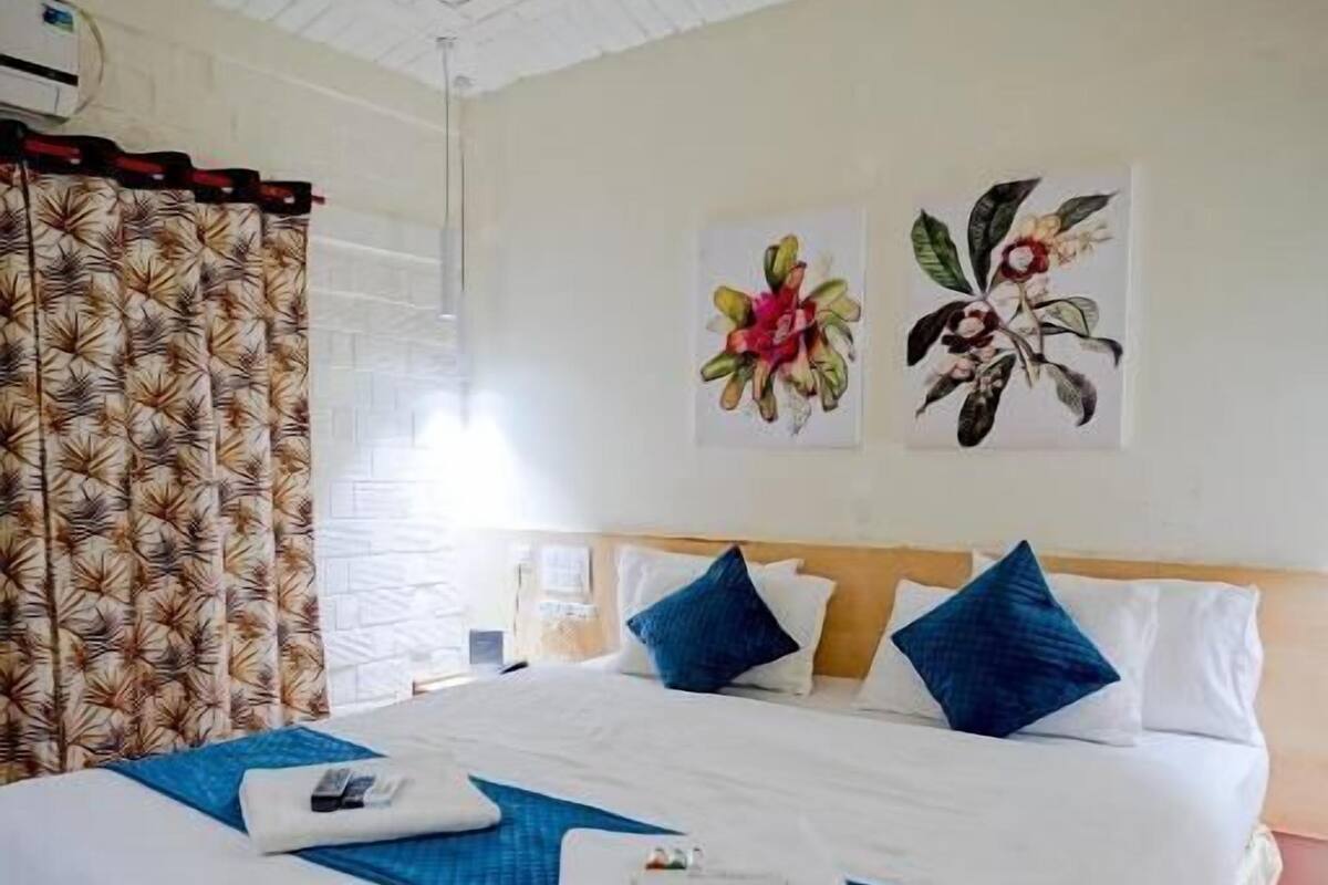 A hotel room with a large bed, white and blue bedding, a wooden headboard, and two floral wall art pieces.
