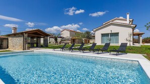 A swimming pool with lounge chairs, a stone structure, and a modern house with a large window. - Jolanda by Interhome (Rovinj/Žminj)