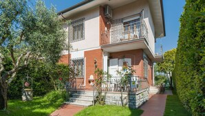 Een herenhuis met een balkon, een stenen trap en een verzorgde tuin.