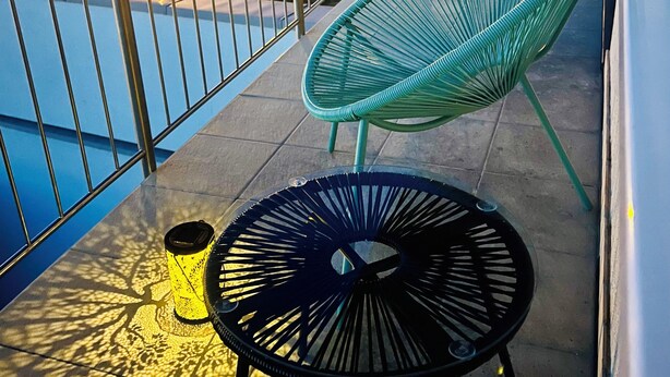 A balcony with a green chair, a small round table, and a yellow cup.