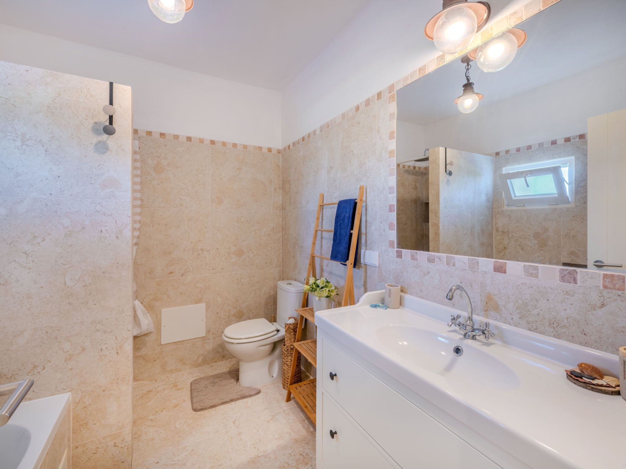 Une salle de bain avec une baignoire, des toilettes et un lavabo. On y trouve un porte-serviettes avec une serviette bleue et une échelle en bois appuyée contre le mur.