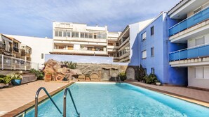 Una piscina con un muro de piedra de fondo, rodeada de edificios de varios pisos con balcones.