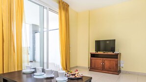 Un comedor con una mesa dispuesta para cuatro, un televisor sobre un mueble de madera y vistas al exterior a través de un ventanal corredero.