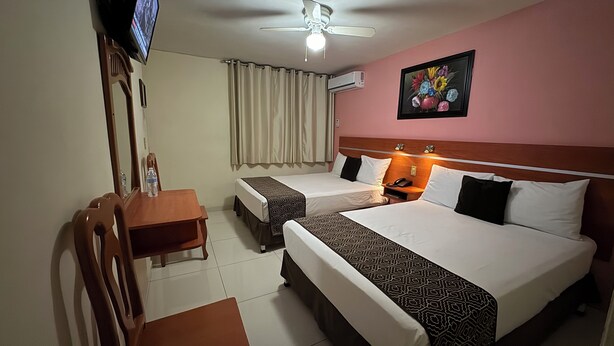 A hotel room with two beds, a desk, a chair, a television, and an air conditioning unit. - Hotel Ana Isabel (Zamora)