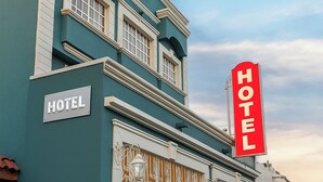 A hotel with a teal facade, a prominent red sign, and a gated entrance. - Hotel Ana Isabel (Zamora)