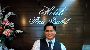 A hotel reception desk with a wooden panel wall, a floral arrangement, and a sign that reads "Hotel Ana Bel." - Hotel Ana Isabel (Zamora)