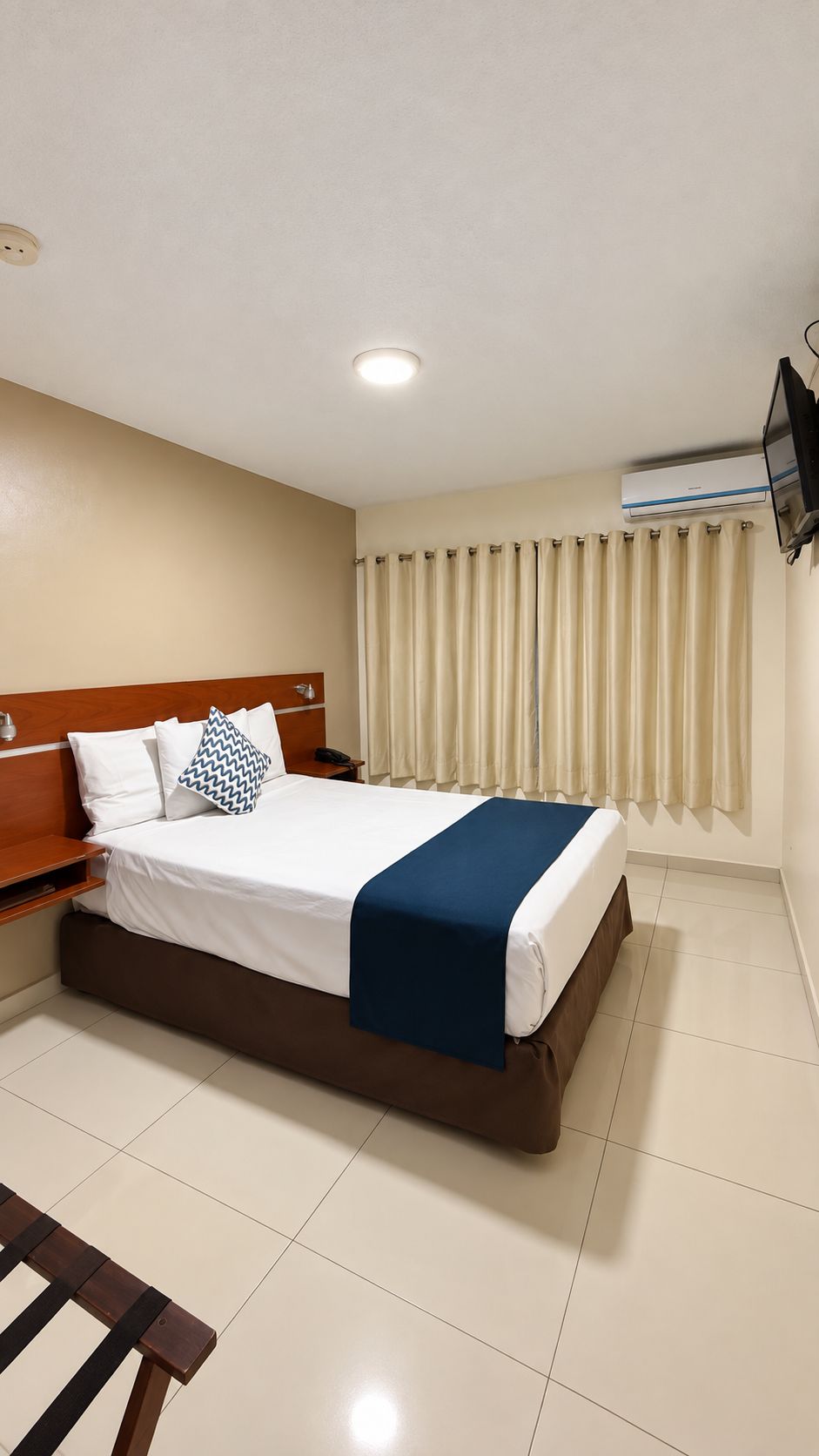 A hotel room with a bed, bedside table, and a flat-screen TV mounted on the wall.