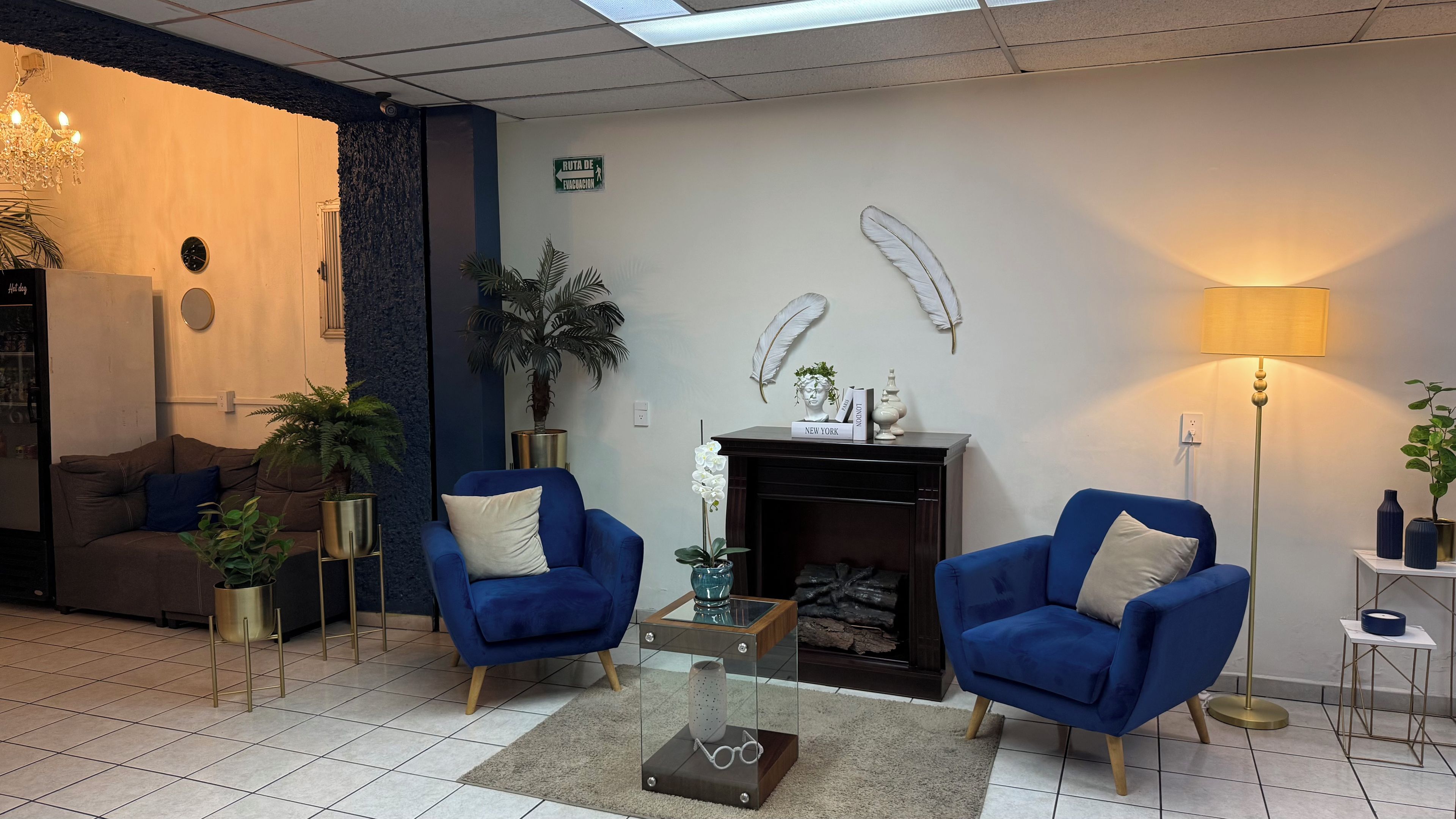 Un salon moderne avec deux fauteuils bleus, une table basse en verre, une cheminée et des objets décoratifs.