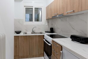 Een kleine keuken met houten kastjes, een wit aanrecht, een spoelbak, een fornuis en een raam.