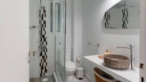 Een moderne badkamer met een glazen douchecabine, een wit toilet, een wastafel met een stenen kom en een spiegel boven de wastafel.