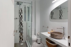 Een moderne badkamer met een glazen douchecabine, een wit toilet, een wastafel met een stenen kom en een spiegel boven de wastafel.