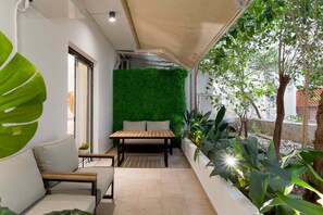 Um pátio moderno com mesa e banco de madeira, rodeado por plantas verdes e um muro vertical coberto de vegetação.