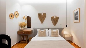 Een moderne slaapkamer met een groot bed, een houten nachtkastje, een spiegel en decoratieve items aan de muur.