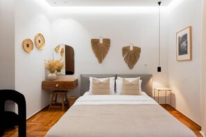 Een moderne slaapkamer met een groot bed, een houten nachtkastje, een spiegel en decoratieve items aan de muur.