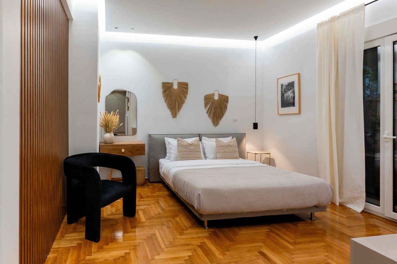 Un dormitorio moderno con cama, una silla, una mesita de noche y un ventanal con cortinas.