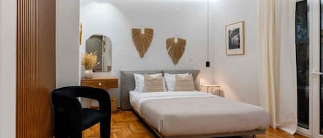Un dormitorio moderno con cama, una silla, una mesita de noche y un ventanal con cortinas.