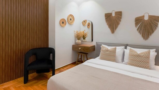 Een moderne slaapkamer met een groot bed, een wandpaneel van hout, een zwarte stoel, een houten bureau en decoratie aan de muur.