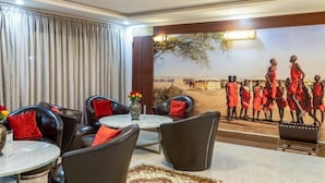 A hotel room with a dining area featuring leather chairs and a round table, a large mural depicting a traditional scene, and a view of a desert landscape. - The Ole-Ken Hotel (Nakuru)