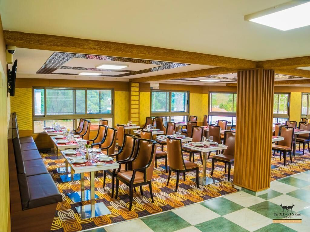 Ein Hotelrestaurant mit mehreren Tischen und Stühlen, einem gemusterten Teppich und großen Fenstern.