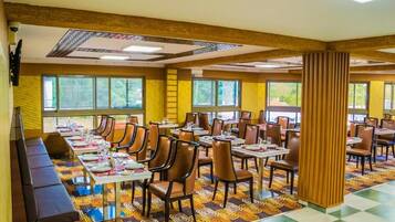 A hotel dining area with multiple tables and chairs, a patterned carpet, and large windows.
