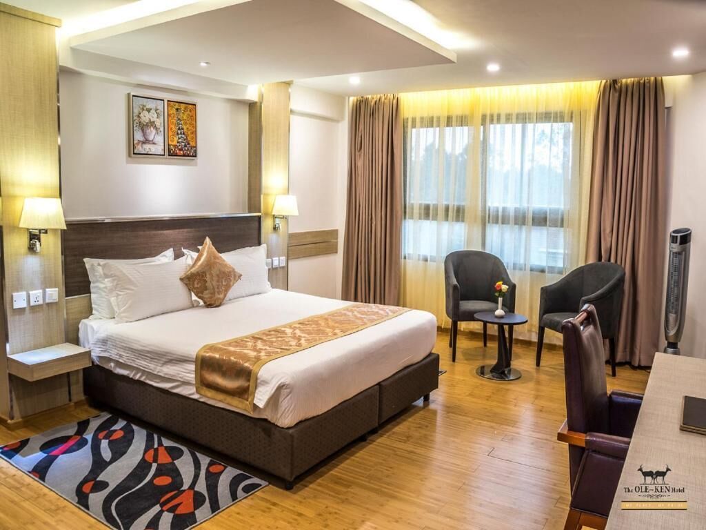 A hotel room with a large bed, two bedside tables, a chair, a small table, and a window with curtains.