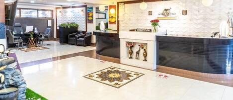 A hotel reception area with a reception desk, seating area, and decorative elements like a fountain and wall art.