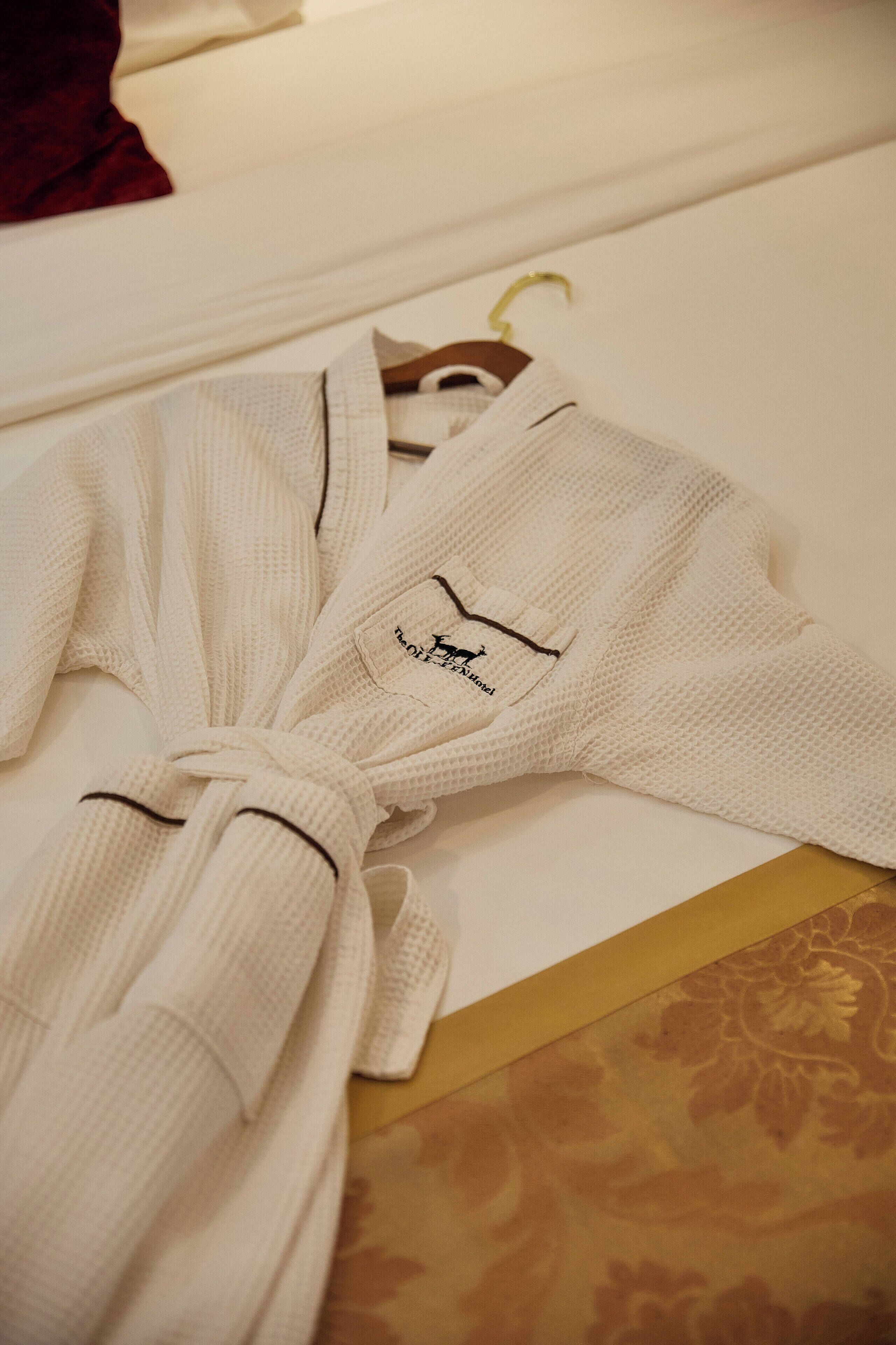 Un albornoz blanco, con un logotipo en la etiqueta interior, ceñido a la cintura, sobre una superficie estampada.