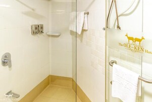Baño de hotel con cabina de ducha de vidrio, lavamanos blanco y barra para toallas.