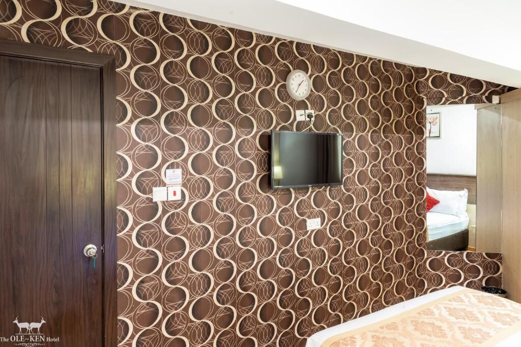Une chambre d’hôtel avec un papier peint à motifs, un téléviseur à écran plat fixé au mur, une armoire en bois et un lit recouvert d’une courtepointe à motifs.