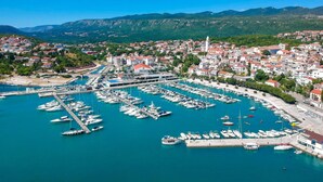 A coastal town with a marina filled with boats, surrounded by residential buildings and green hills in the background.