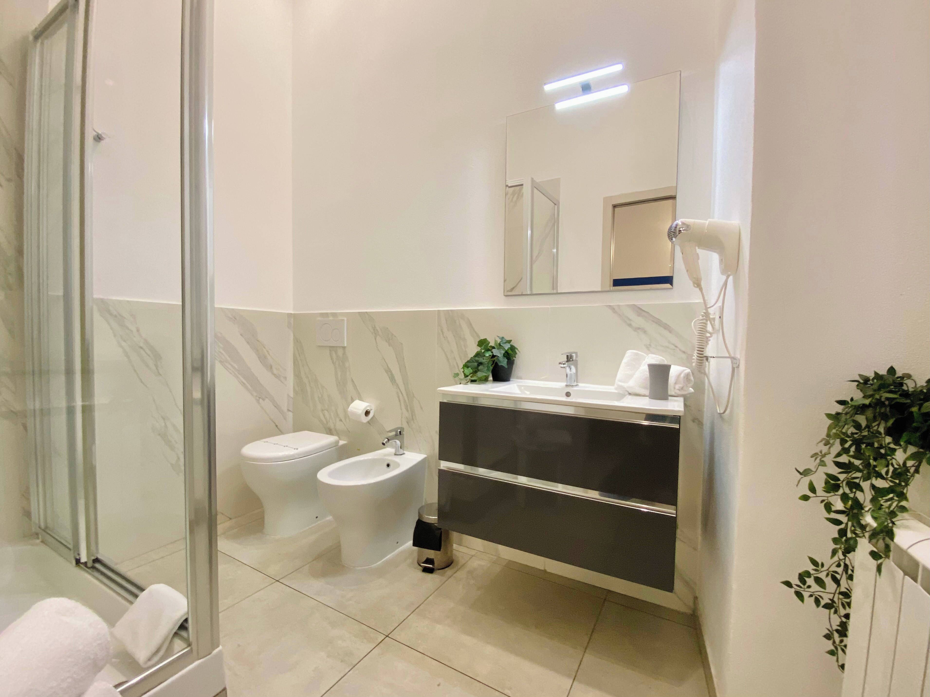 A modern bathroom with a glass shower enclosure, a bidet, a sink with a mirror, and a towel rack.