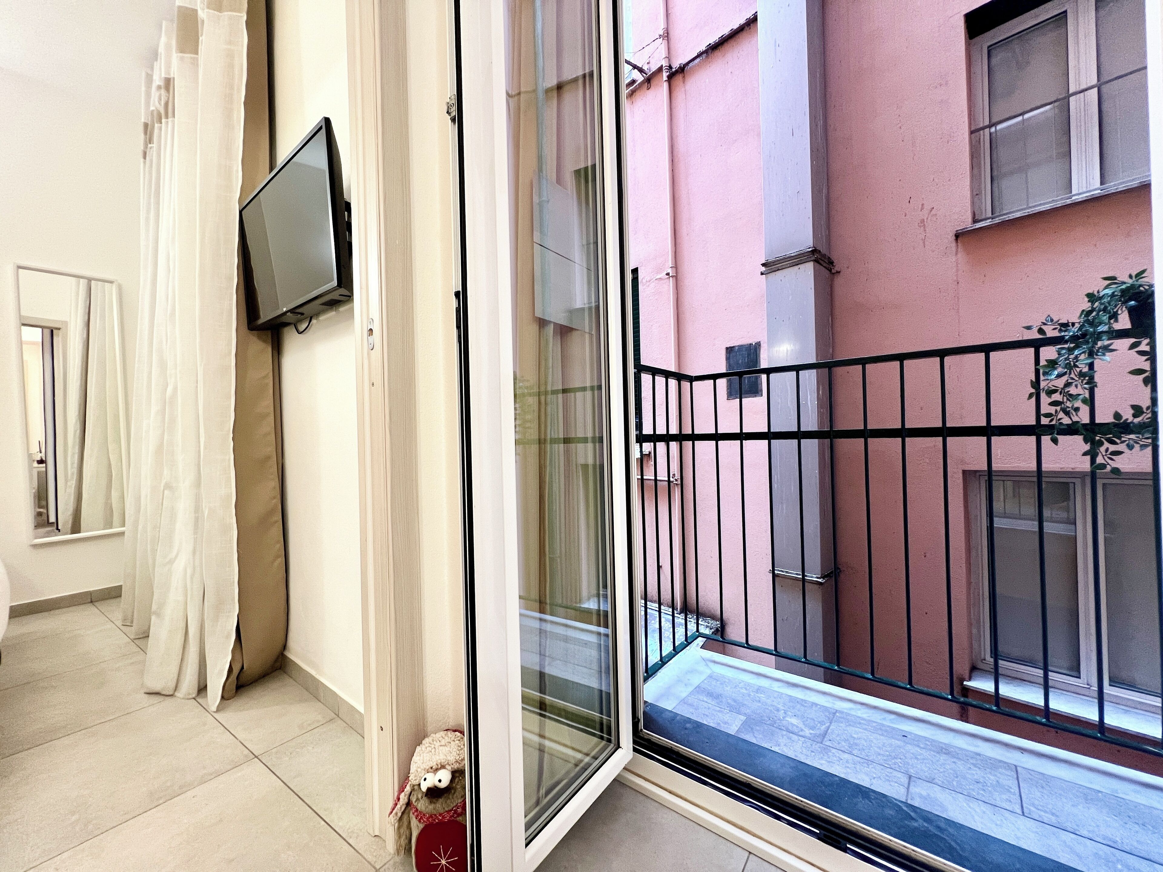 A corridor with a sliding glass door leading to a balcony with a black metal railing.