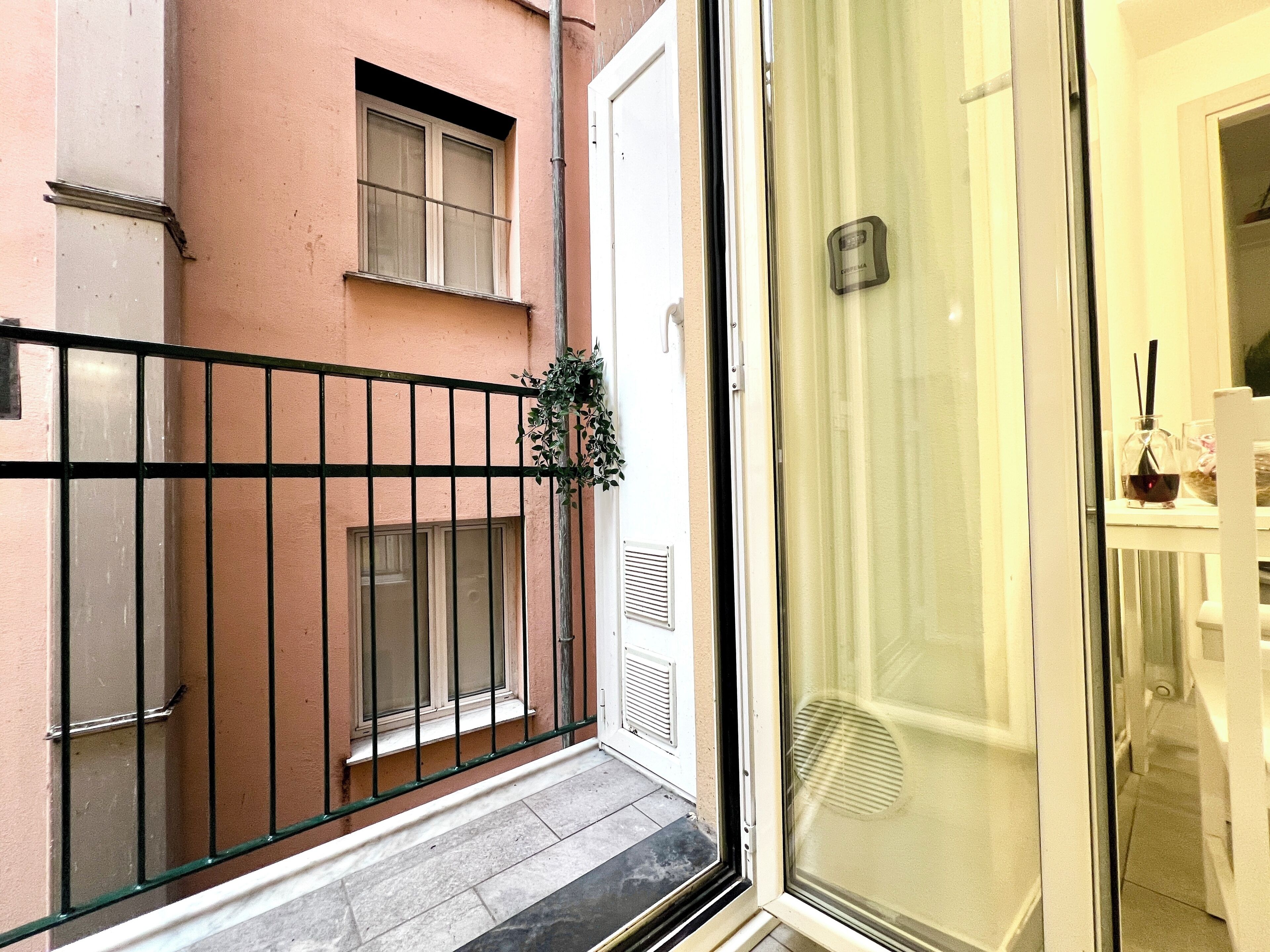 A balcony with a metal railing, a potted plant, and a glass door leading into a room.