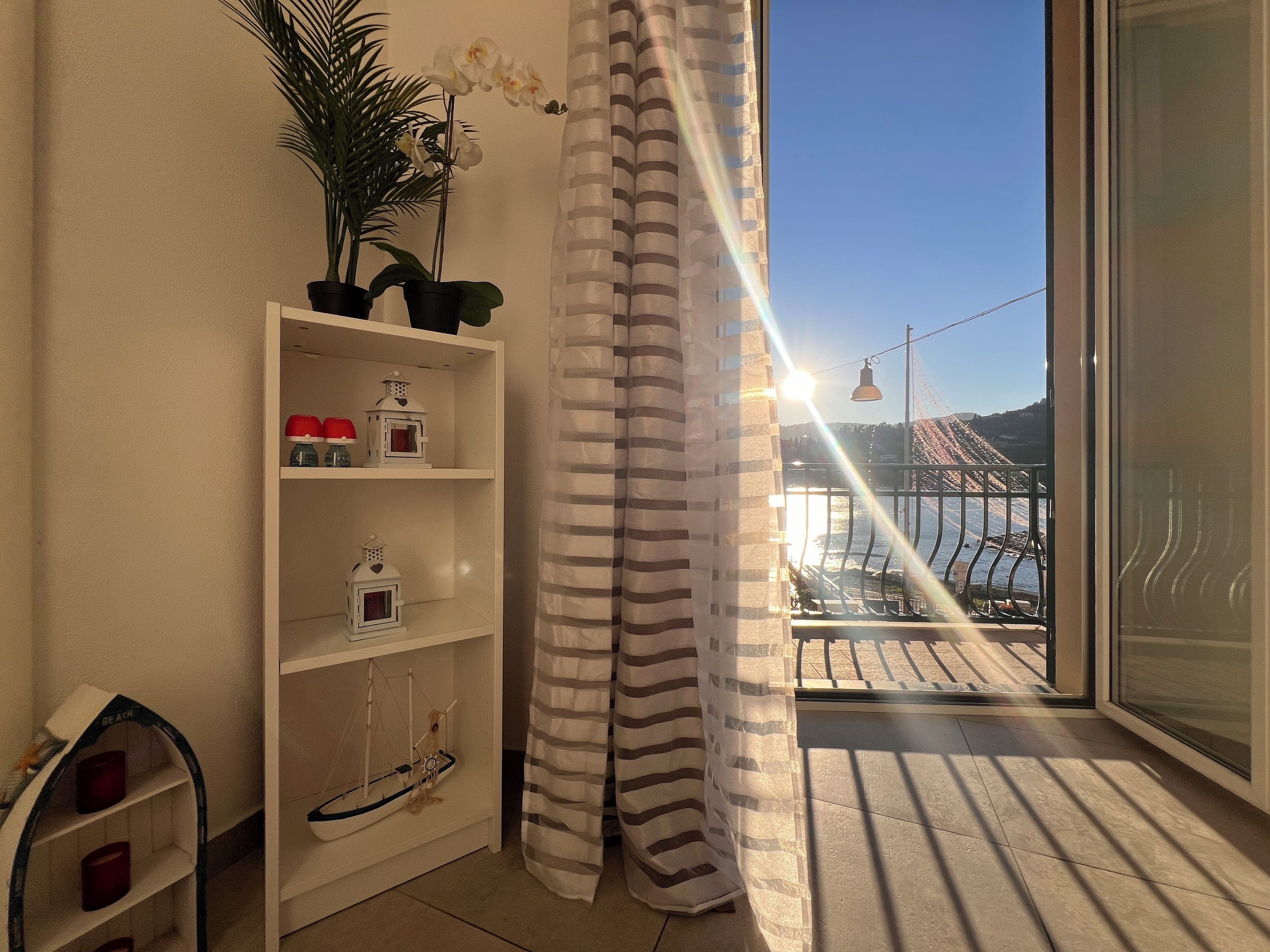 En balkong med utsikt över en bro och vatten, en randig gardin och en hylla med dekorativa föremål.
