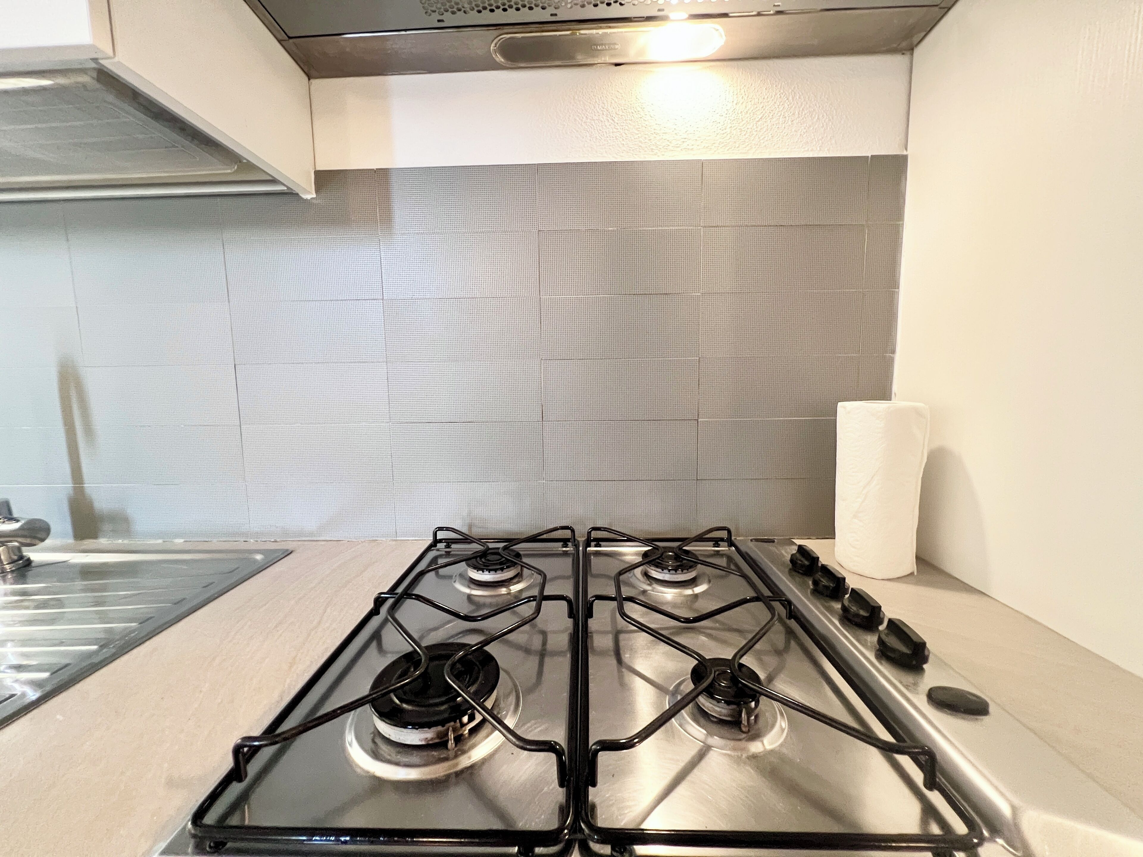 Een keuken met een gasfornuis met vier branders, roestvrijstalen apparatuur en een betegelde spatwand.