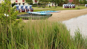 A riverside area with boats, a row of houses, and a grassy bank. - All Inclusive Apartment in Wangerland Resort (Wangerland)