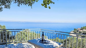 Un banc en pierre, avec une bouteille et un verre, offrant une vue sur la côte, agrémentée d’une balustrade et de verdure.