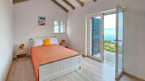 Une chambre avec un lit, une table de chevet, une fenêtre et une porte-fenêtre coulissante donnant sur un balcon avec vue sur la mer.