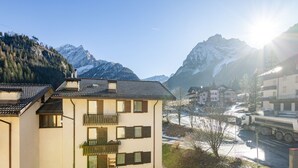 Un edificio de varios pisos con balcones, un pequeño jardín y vistas a montañas nevadas.