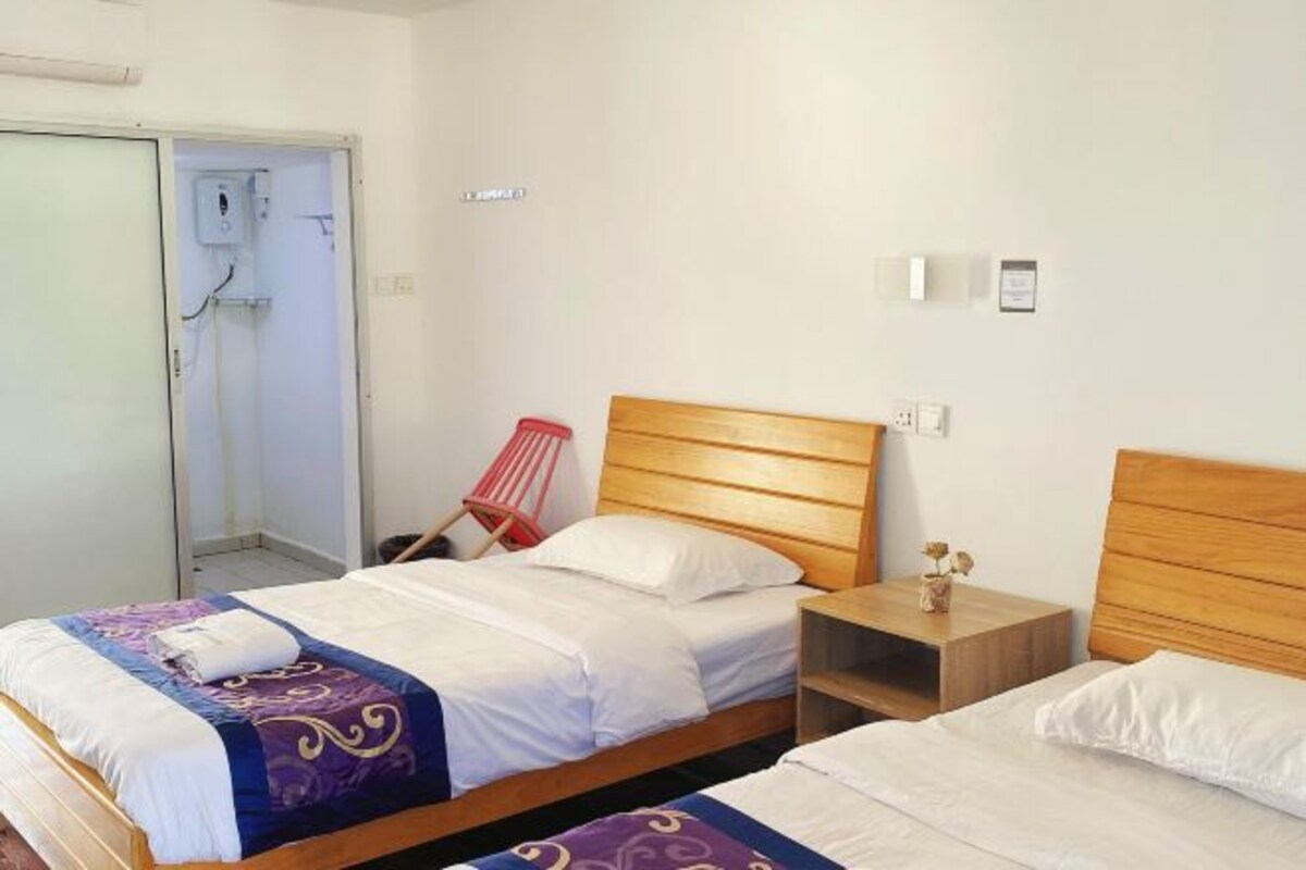 Quarto de hotel com duas camas, cabeceira de madeira, mesa de cabeceira e uma cadeira vermelha.
