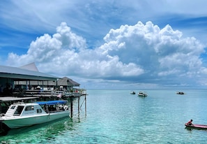 A boat docked at a pier with a building in the background. - Amina Holidays (Mabul Island)