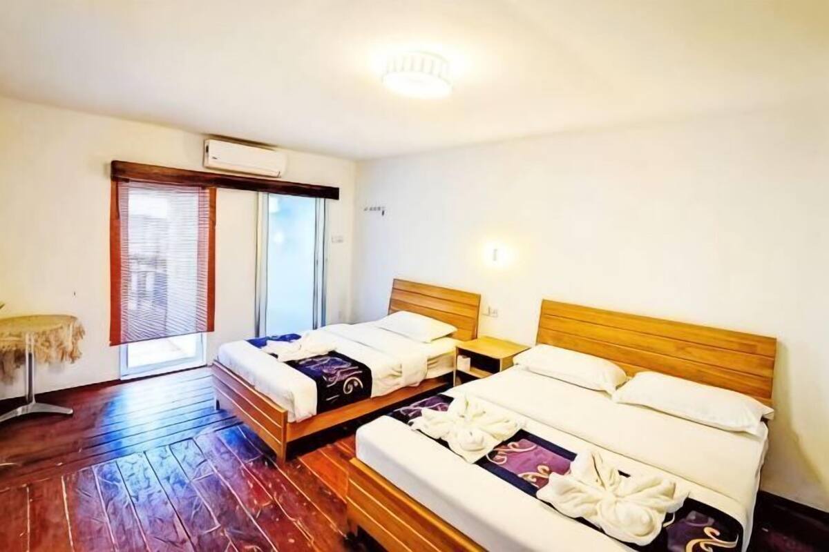 A hotel room with two beds, a small table, a chair, and a window with blinds.
