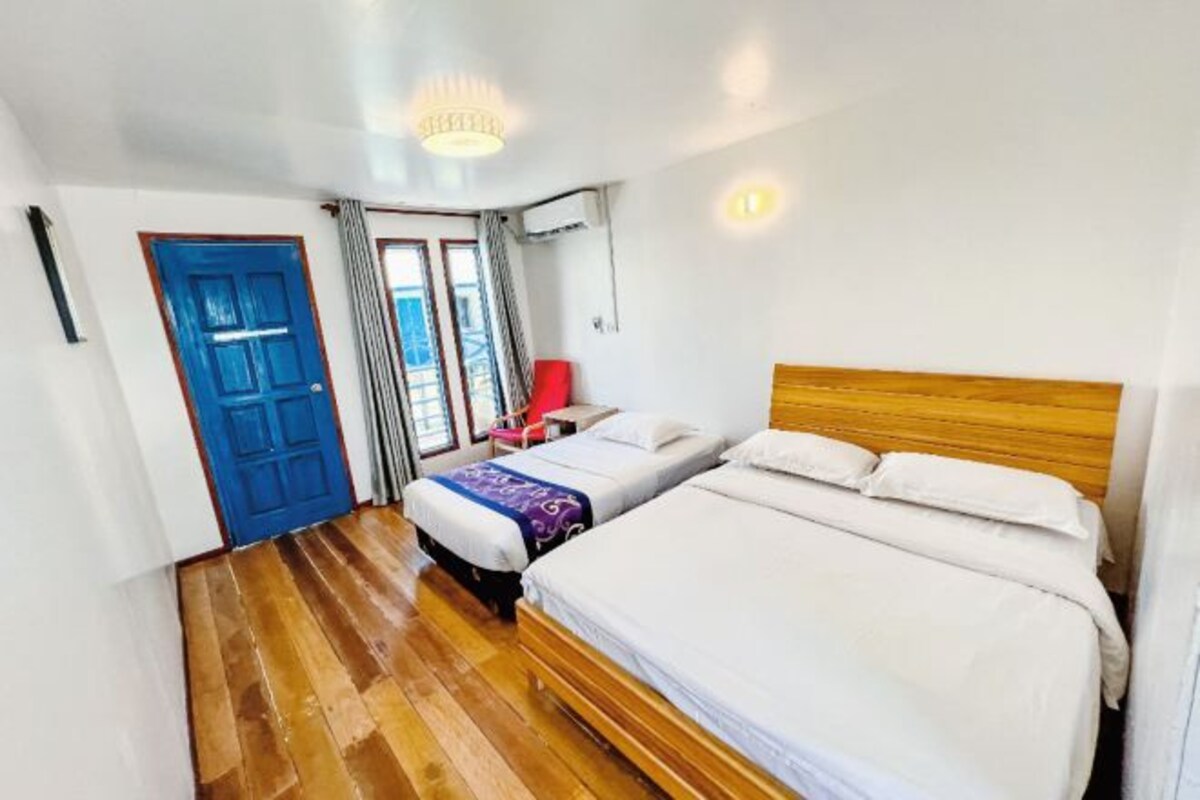 Quarto de hotel com duas camas, piso de madeira, porta azul e um candelabro.