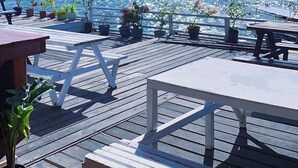 En træterrasse med borde og stole med udsigt over et roligt hav med både.